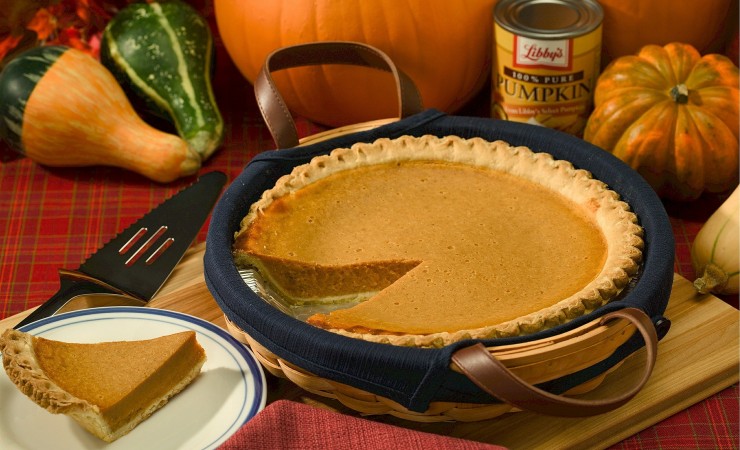 Pumpkin pie in basket alongside decorative gourds on table